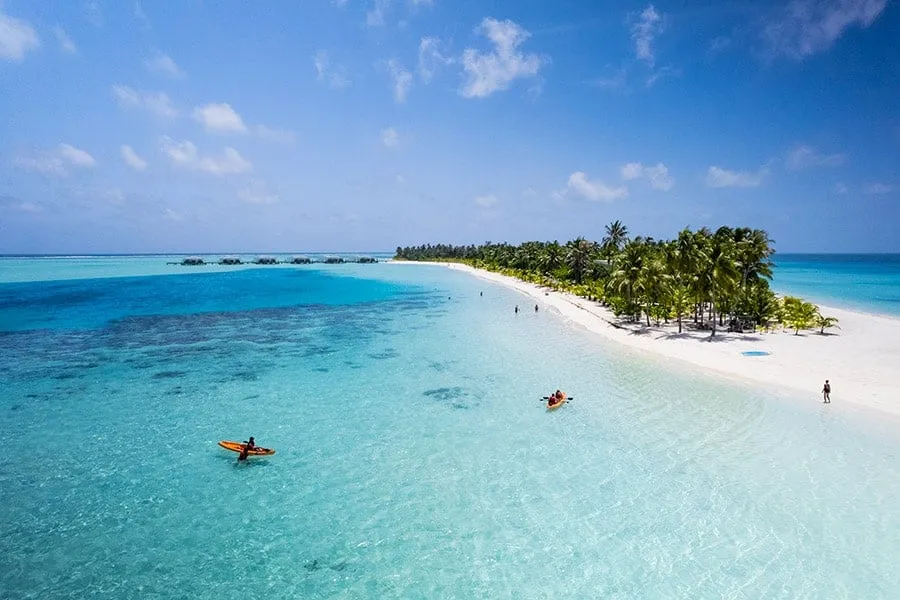 The sandbank at the tip of the island, with 2 people kayaking in the shallows.
