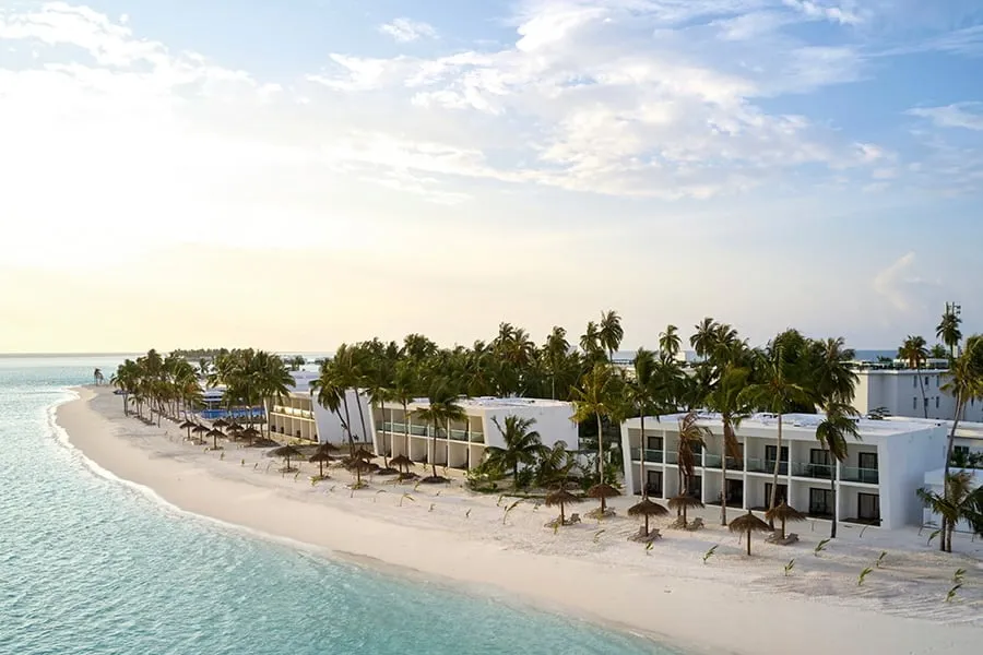 The white buildings of the beach rooms, with thatched parasols on the sand, in early light.