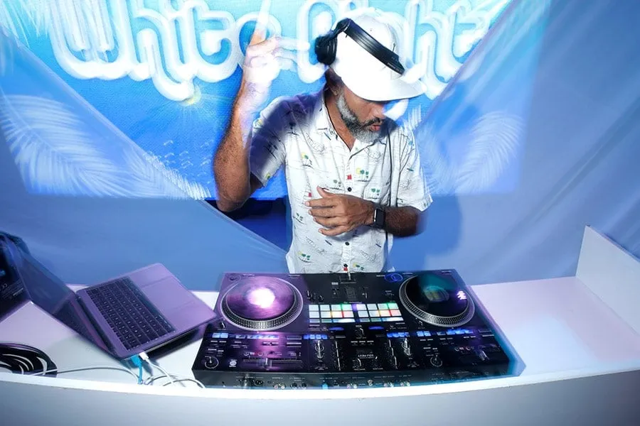 A DJ at the decks during the White Party, in a white hat.