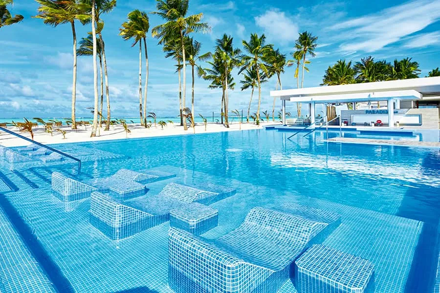 The infinity pool with its submerged loungers, the swim-up bar behind and the palms along the beach.