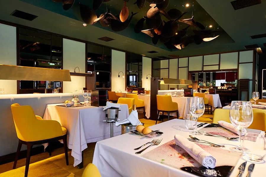Krystal’s dining room, with yellow armchairs, white tablecloths and dark sculptures on the ceiling.
