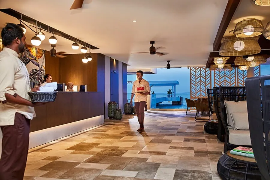 Reception: the wooden desk, the rattan lamps and a member of staff with a basket, with the sea at the far end.