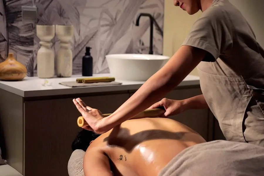 A massage with bamboo rods in a spa room, with the stone basin and the bottles of oil on the counter.