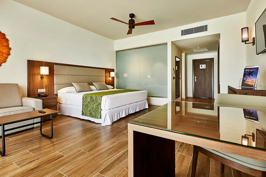 A Jr. Suite with its king bed, sofa and desk, and the glass door open onto the balcony and the sea.
