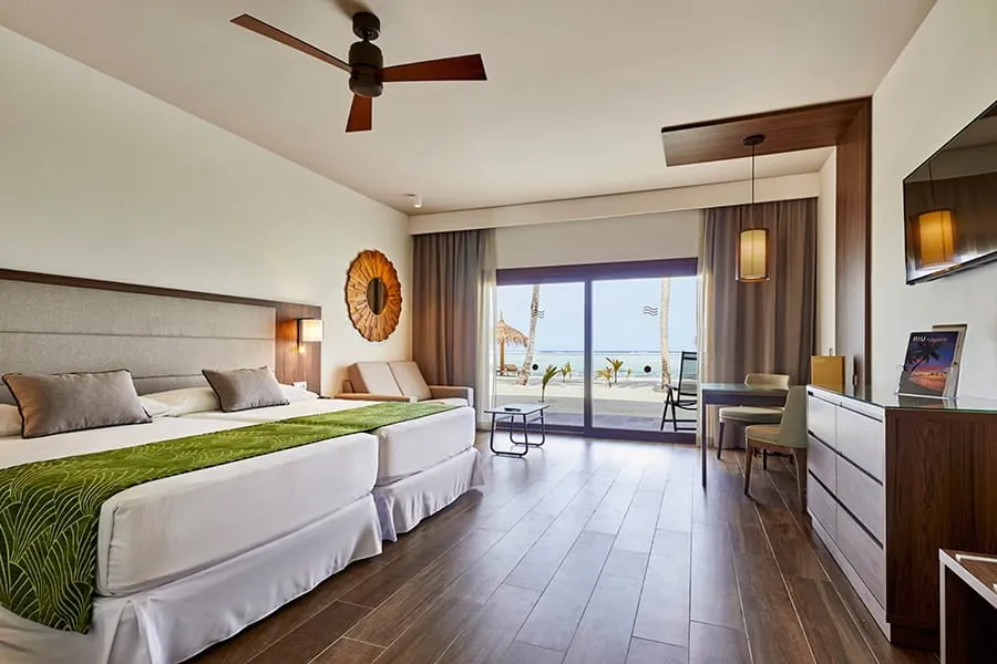 A Junior Suite with beach access, with 2 beds, a ceiling fan and the door open onto the patio and the sand.
