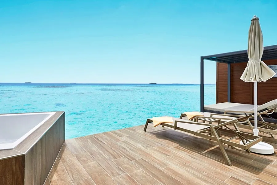 An overwater Suite’s deck, with its outdoor bathtub, loungers, the Balinese bed under its canopy and the open sea.