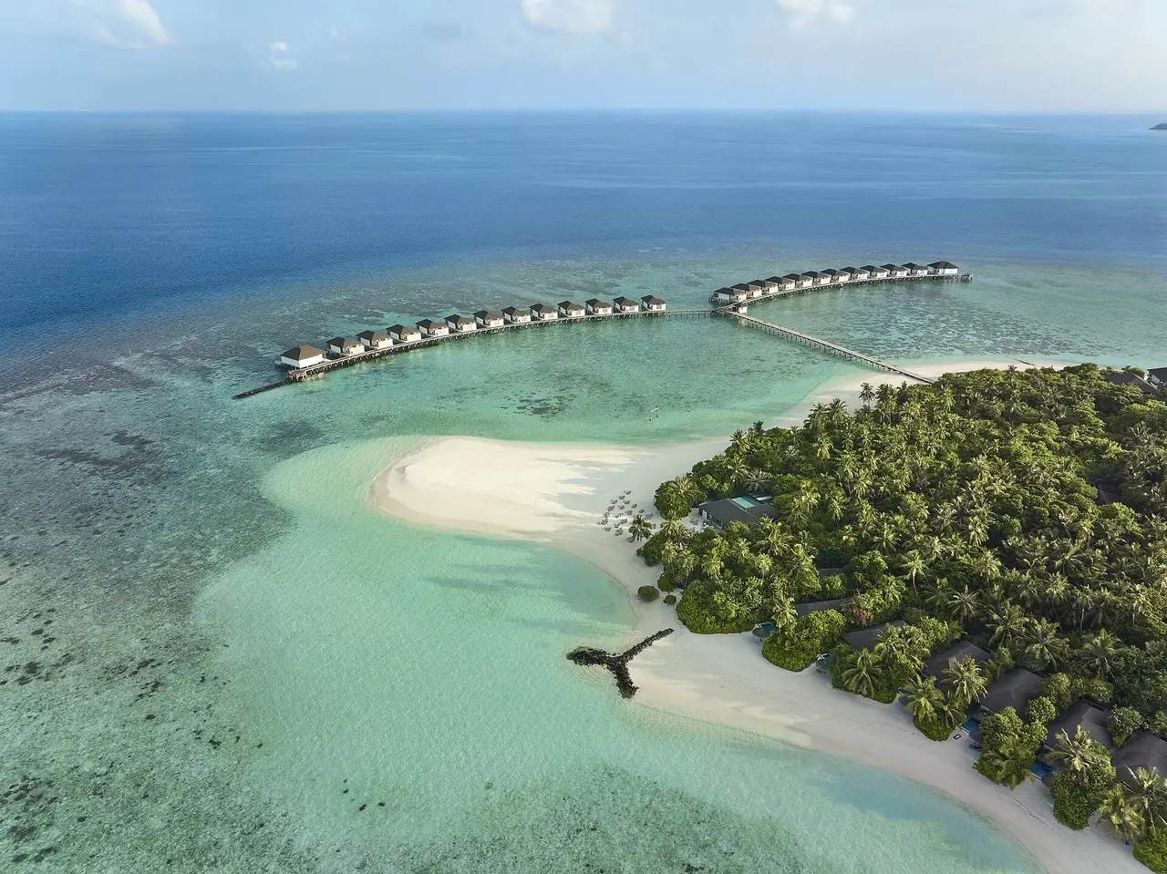 Orivaru from above: the green island with its white spit of sand, the pale lagoon and the 2 jetties of water villas reaching for the open sea.
