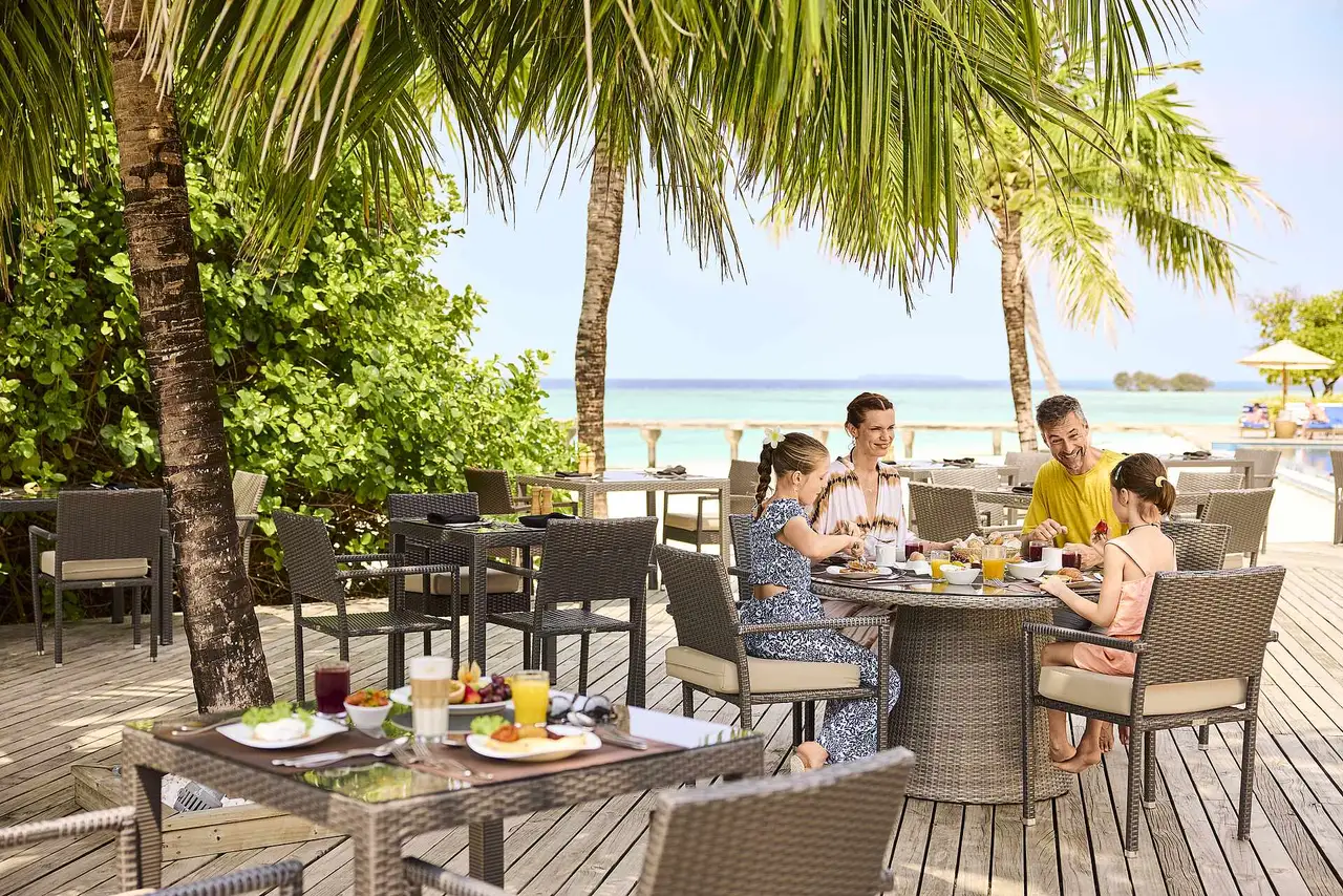 The main restaurant terrace under the palms, with tables laid for breakfast and the sea behind.