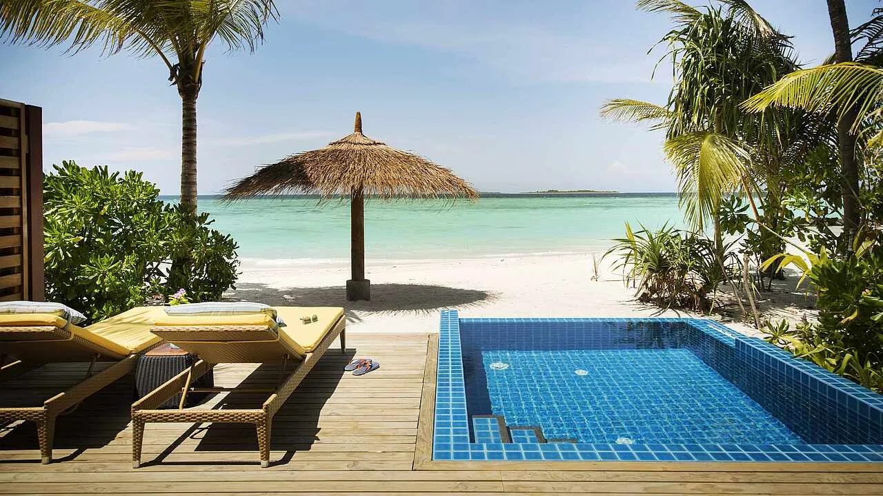 The private pool of a Beach Villa Pool on its deck, with loungers, a thatched parasol and the beach right in front.