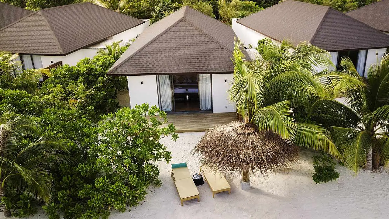A Beach Villa Private Pool from above: the pitched roof among the palms, the loungers and the thatched parasol on the sand.