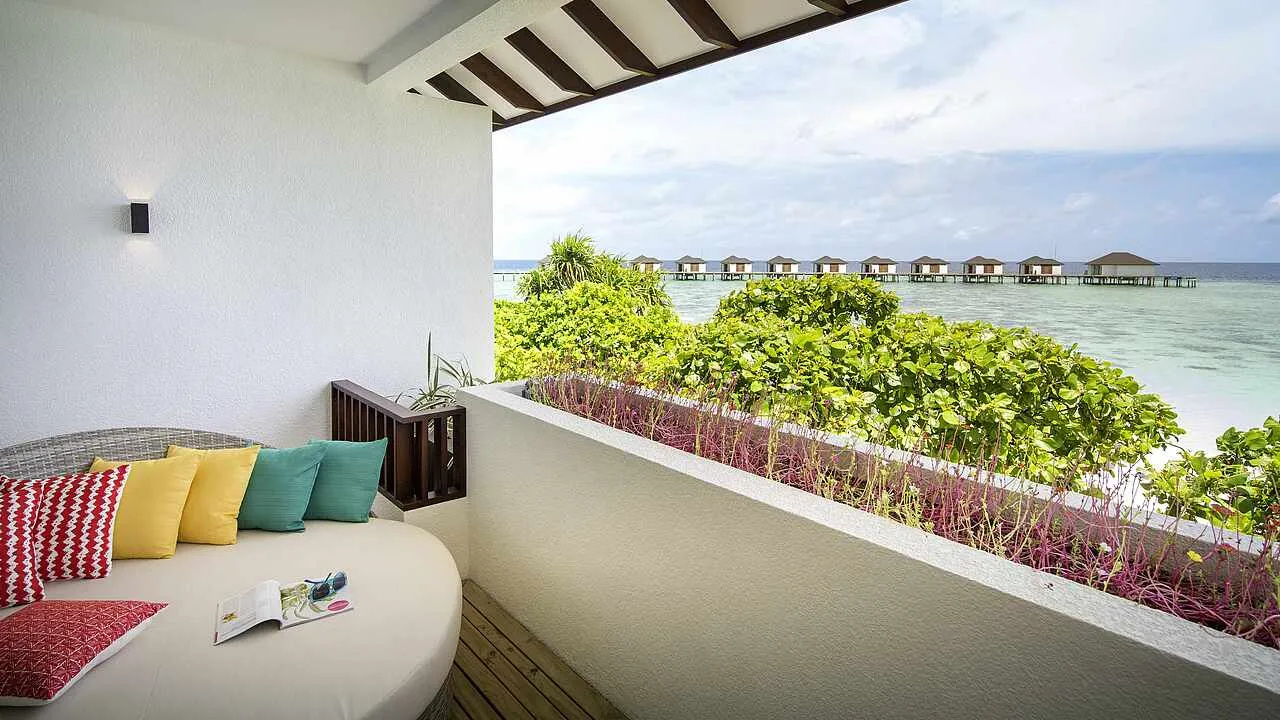 The first-floor balcony of a Double Room Classic Sea View, with its round daybed, bright cushions and the water villas in the distance.