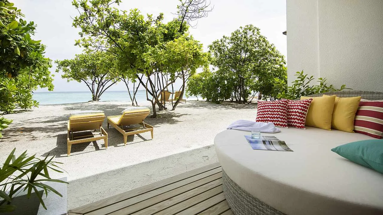 The ground-floor terrace of a Double Room Superior Sea View, with its round daybed and loungers on the sand under the trees.