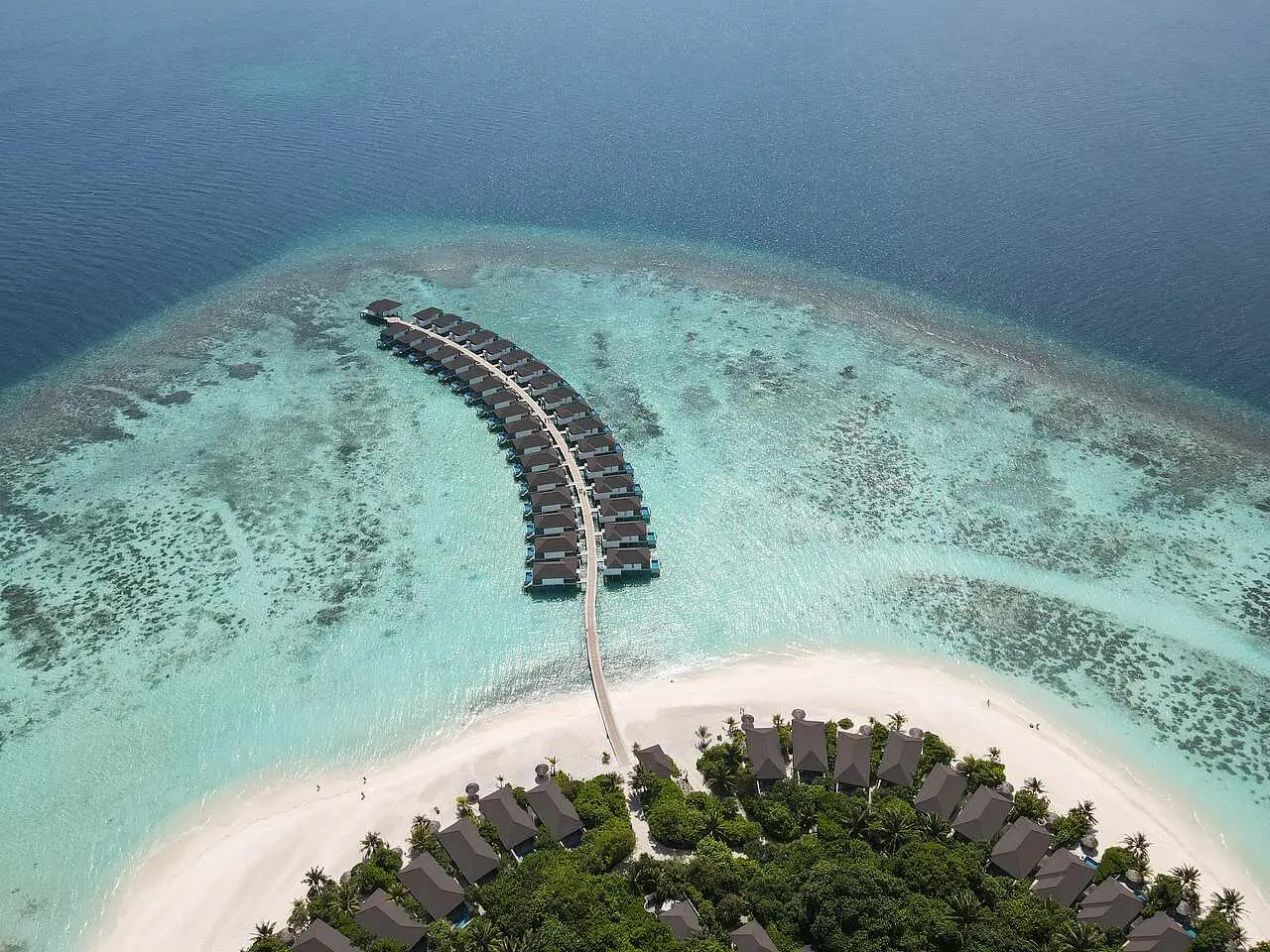 The curving jetty of the Water Villas from above, running from the beach across the lagoon towards the reef.