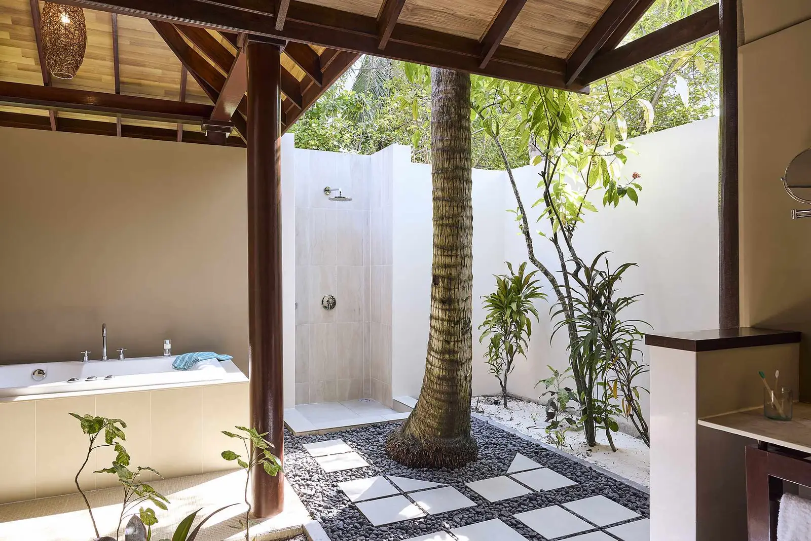The open-air bathroom of a beach villa, with its bath, shower and a palm trunk in the middle of the courtyard.