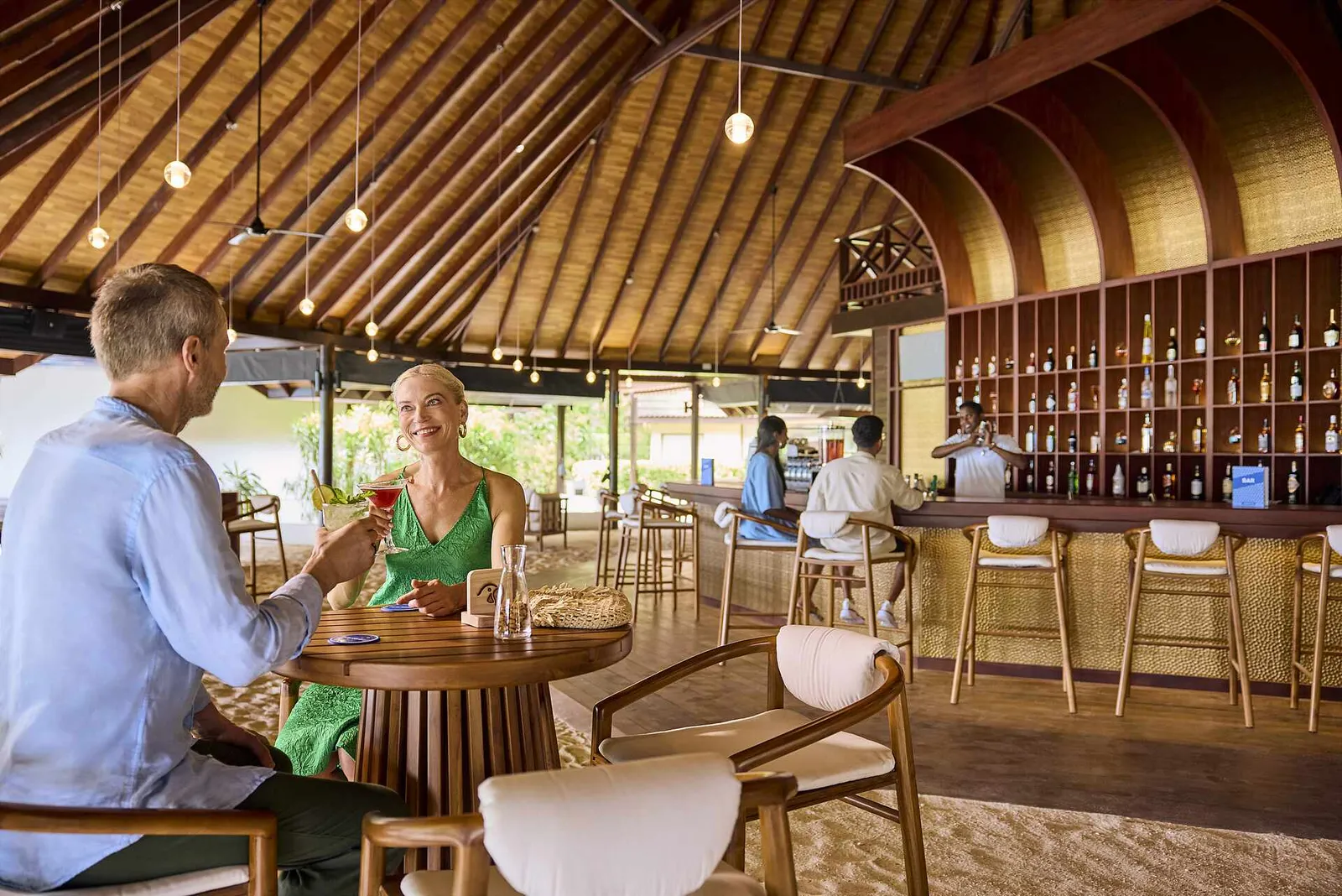 A couple raise their glasses at a table in the main bar, under the great timber roof, with the counter and bottles behind.