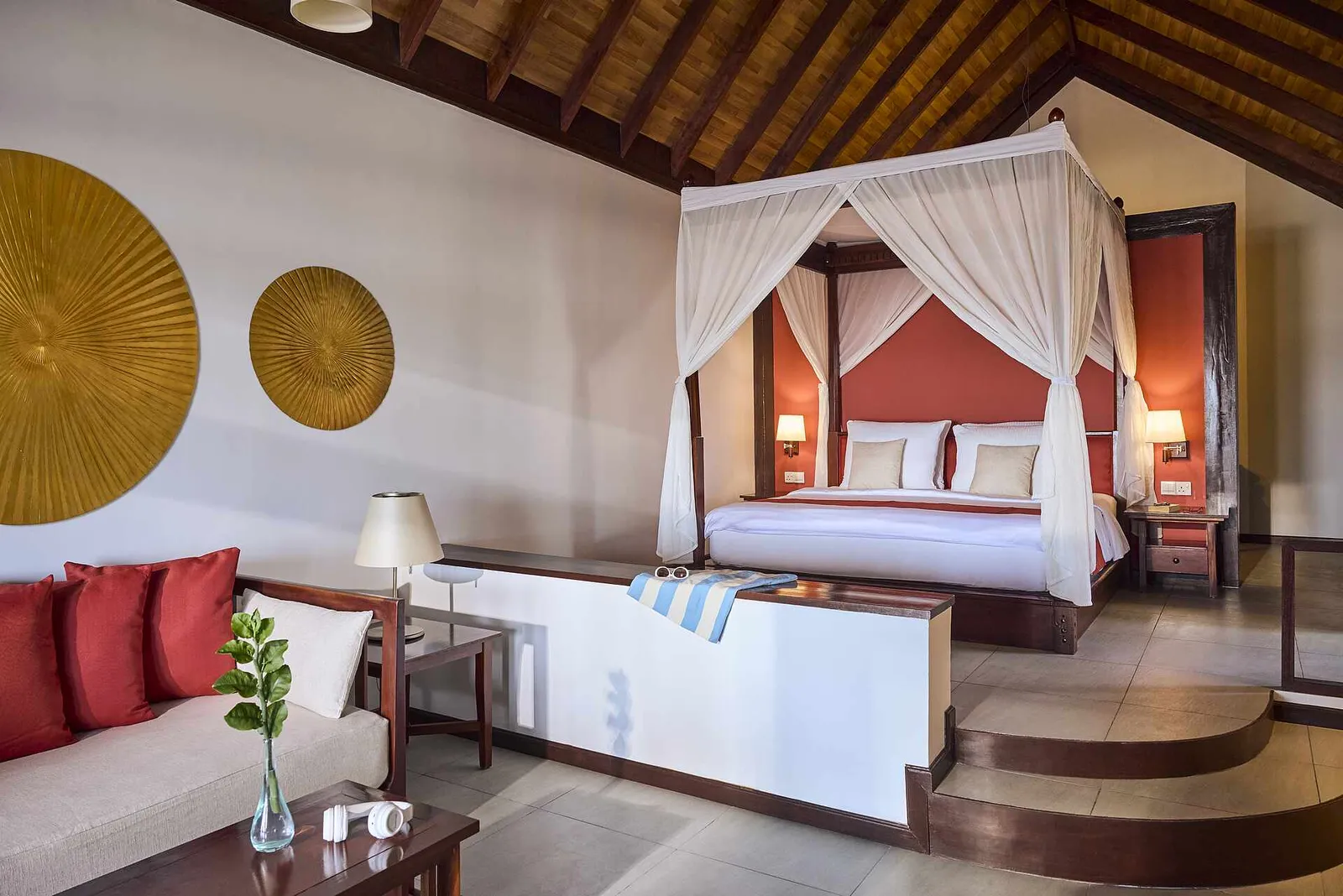 A Beach Villa Classic Sea View: the four-poster with white curtains, the 2 steps and the red sofa.