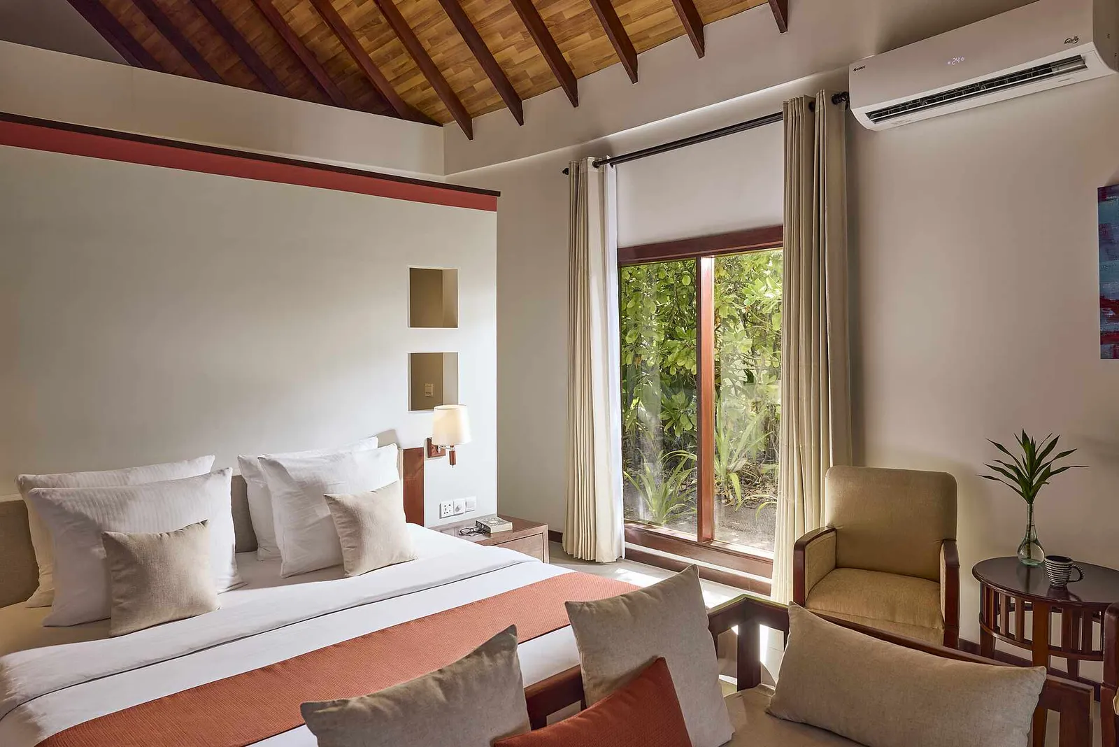 A Beach Villa Superior Sea View bed under the timber ceiling, with an armchair and the window onto the green.