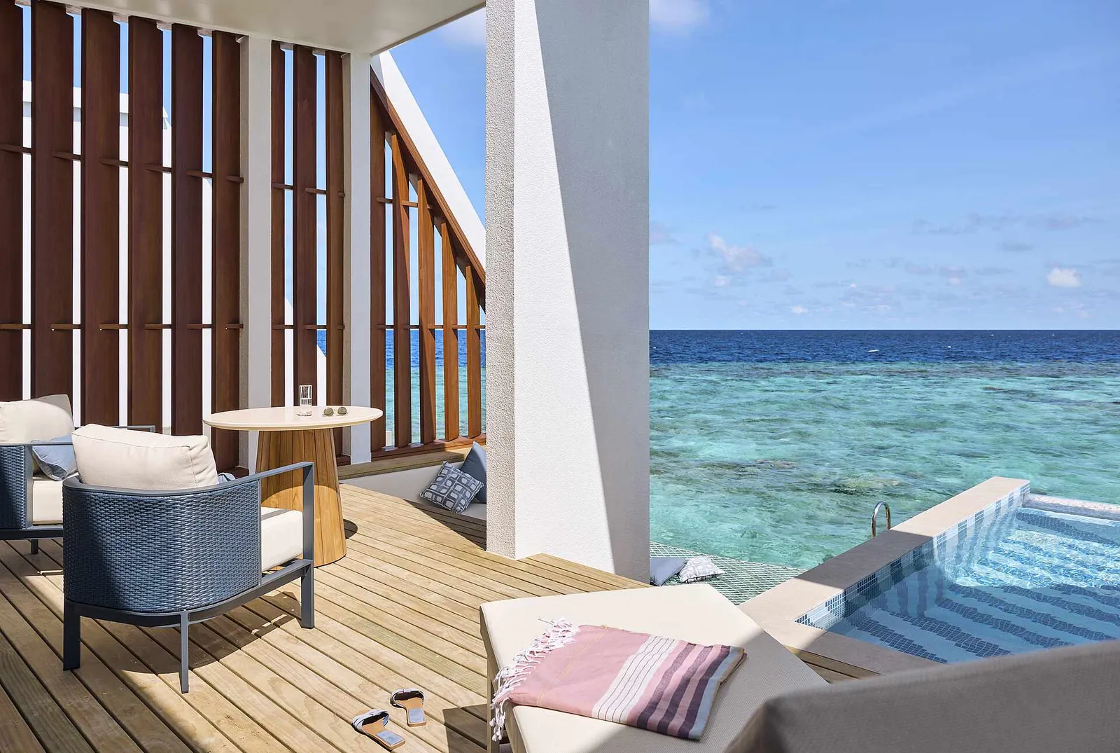 The deck of an Exclusive Reef Water Villa Pool: table, chairs, the daybed and the pool on the edge of the reef.