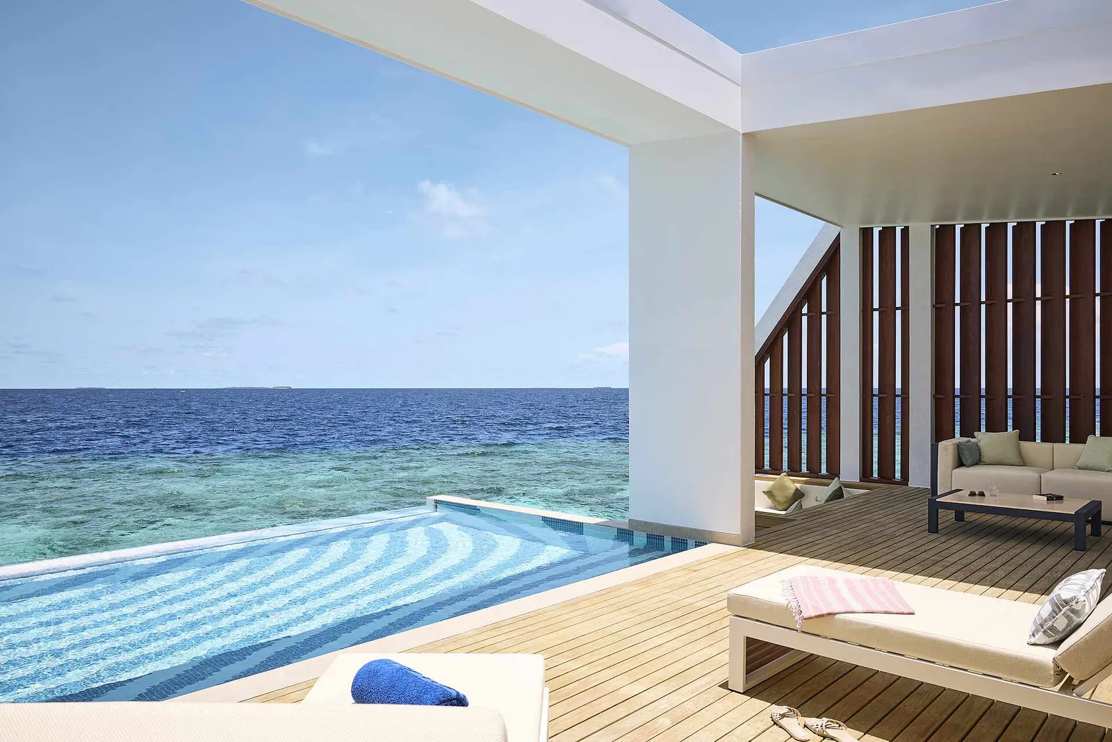 The deck of the Funamadua One Bedroom Water Villa Pool, with its blue-striped infinity pool and the open-air lounge.