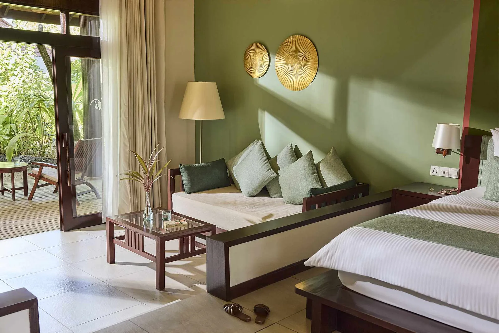 A Villa Classic Garden View bedroom: the bed, the cushioned bench under 2 golden discs and the door onto the garden.