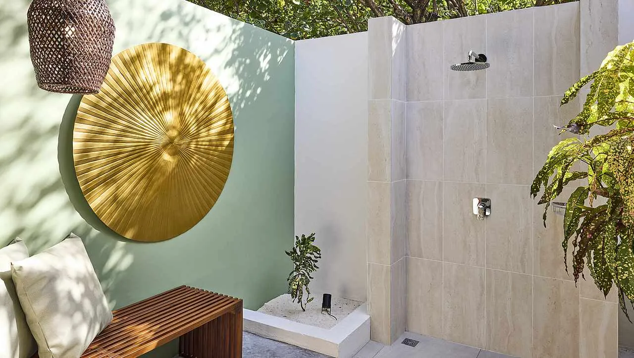 The open-air shower of a Villa Economy, between pale walls, a golden disc and the garden plants.