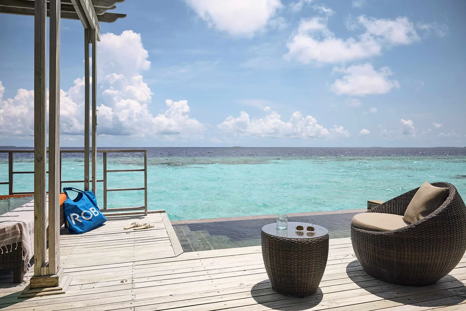 The deck of a Water Villa Classic Private Pool, with wicker chairs, the pool and the turquoise lagoon.