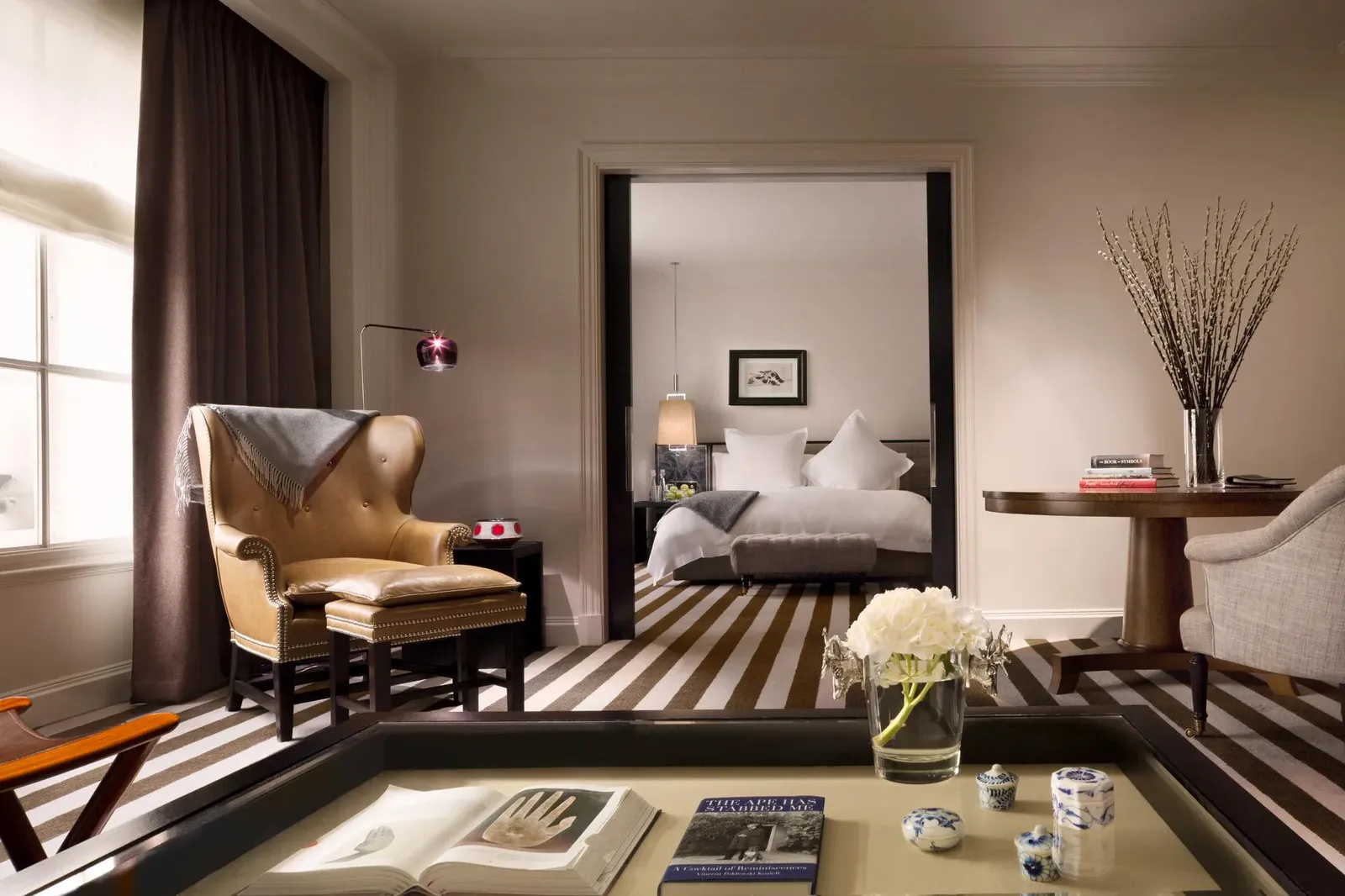 A Deluxe Suite’s sitting room: a tan leather armchair, a low table with white flowers and the bedroom beyond the door