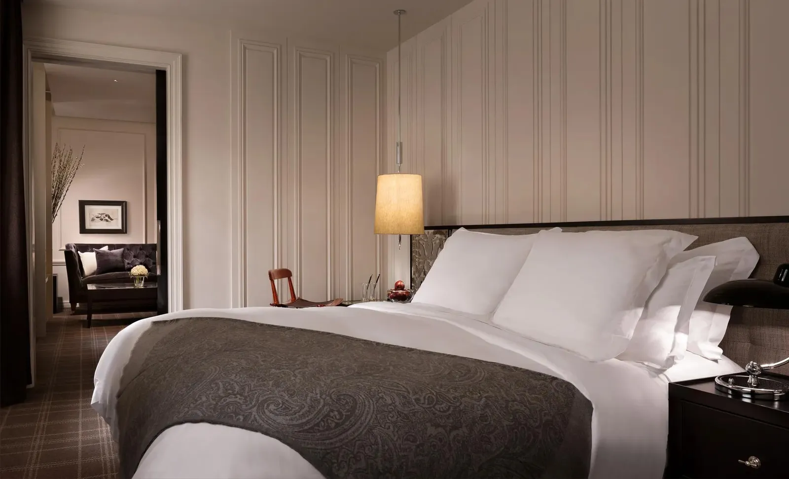 A Premier Suite’s bedroom: a white bed with a grey cover, dark bedside tables and the sitting room beyond
