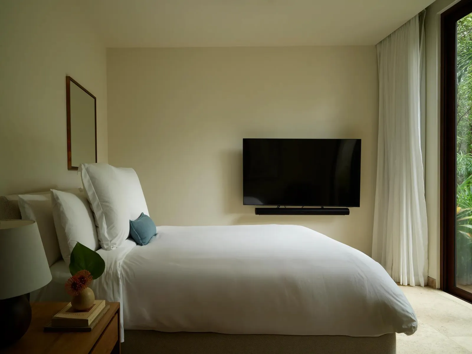 A bedroom with a bed and television, lit from the window