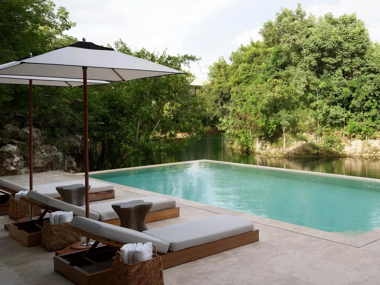 The pool with a parasol and loungers in front of the greenery