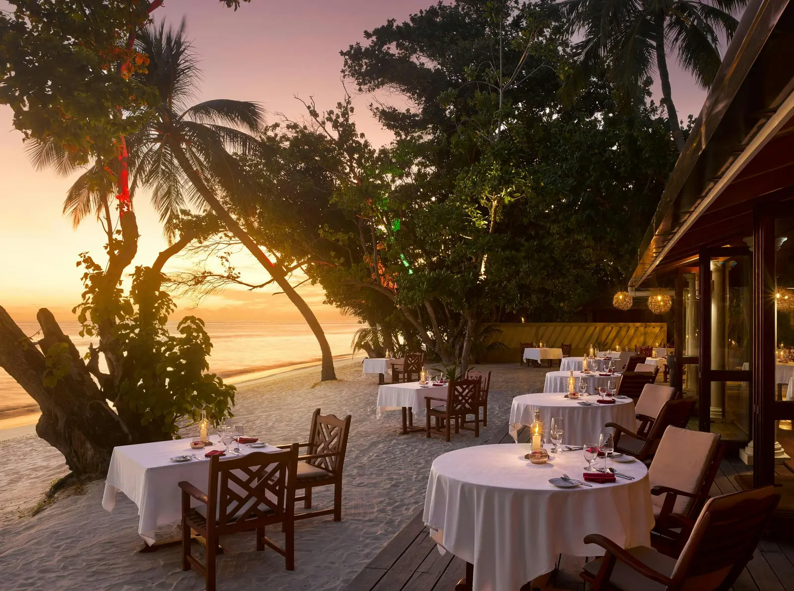 Raabondhi’s tables laid on the sand among the trees, with the sun setting over the sea.