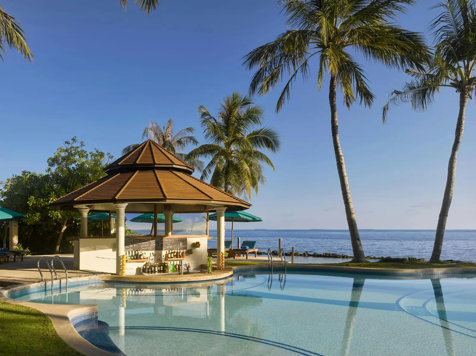 The Pool Bar under its pagoda roof in the middle of the pool, with palms and the sea behind.
