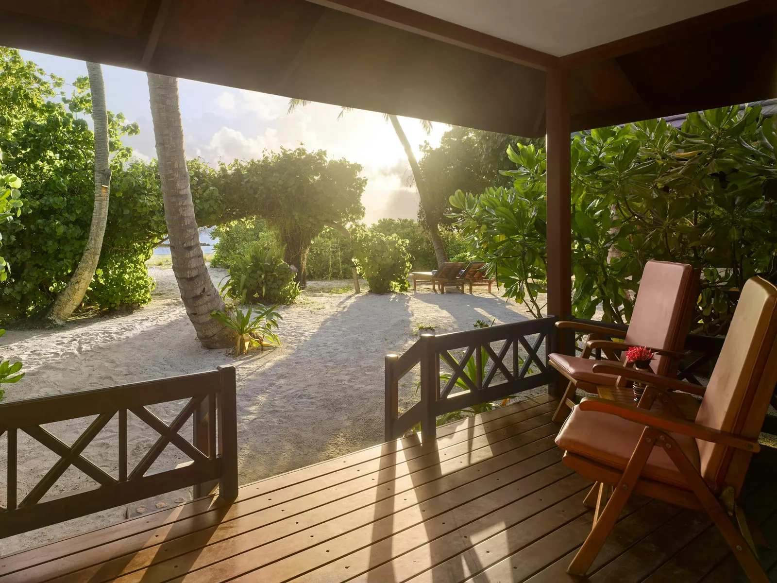 A Sunset Beach Villa’s veranda in the evening light, with timber chairs and the path through the green.