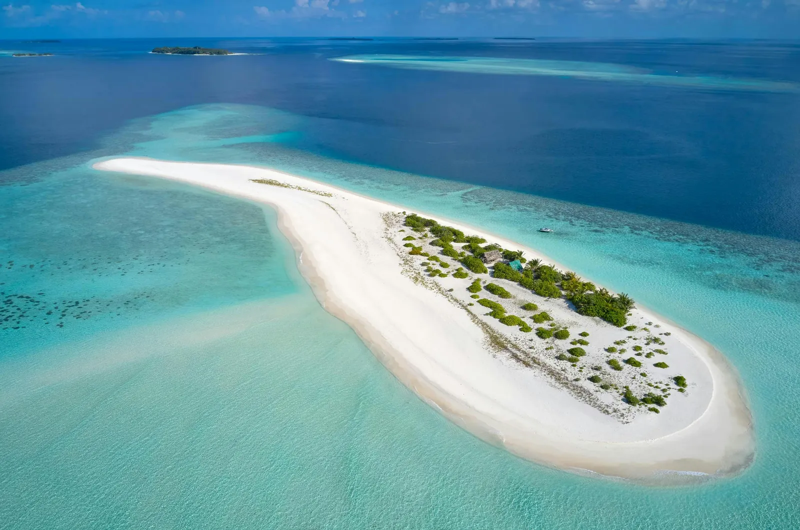 A white sandbank from above, with a patch of scrub, in the turquoise water of the atoll.