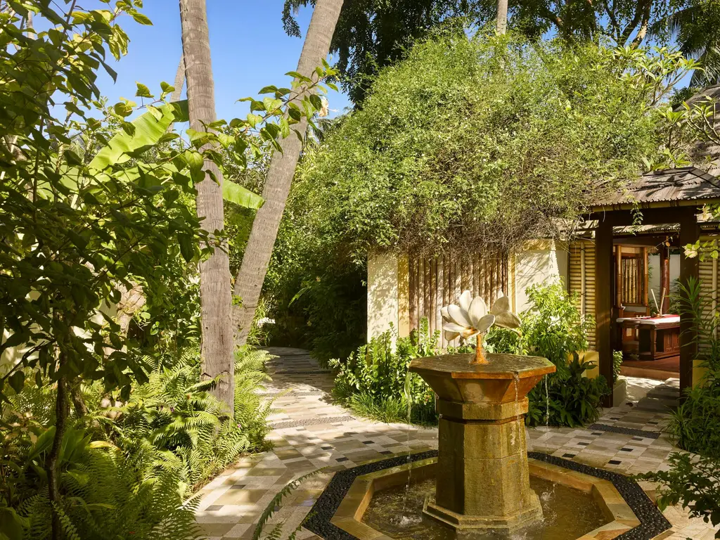 The Araamu Spa courtyard with its stone fountain, the path and the rooms among the palms.