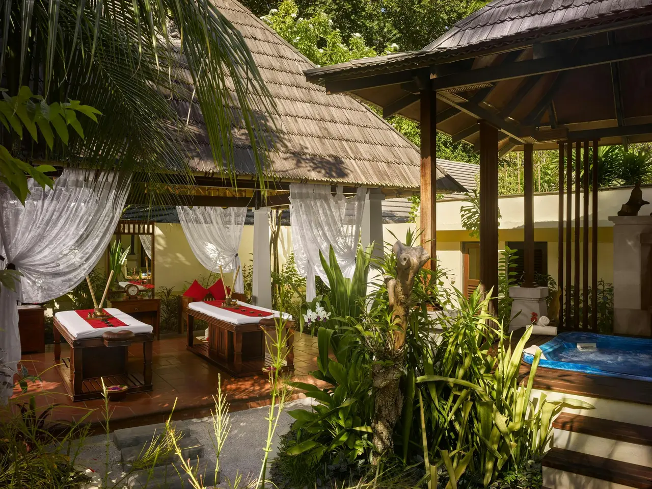 An Araamu Spa room open to the garden, with 2 treatment beds, white curtains and a tub among the plants.