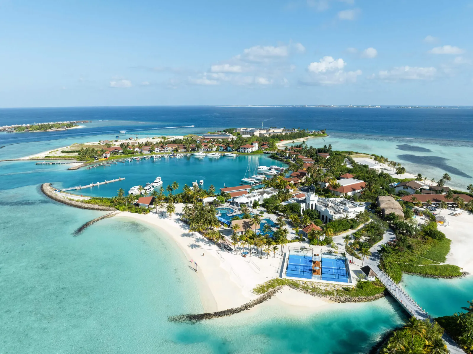 CROSSROADS from the air: the marina and its boats, the white beach, the 2 padel courts and the footbridge