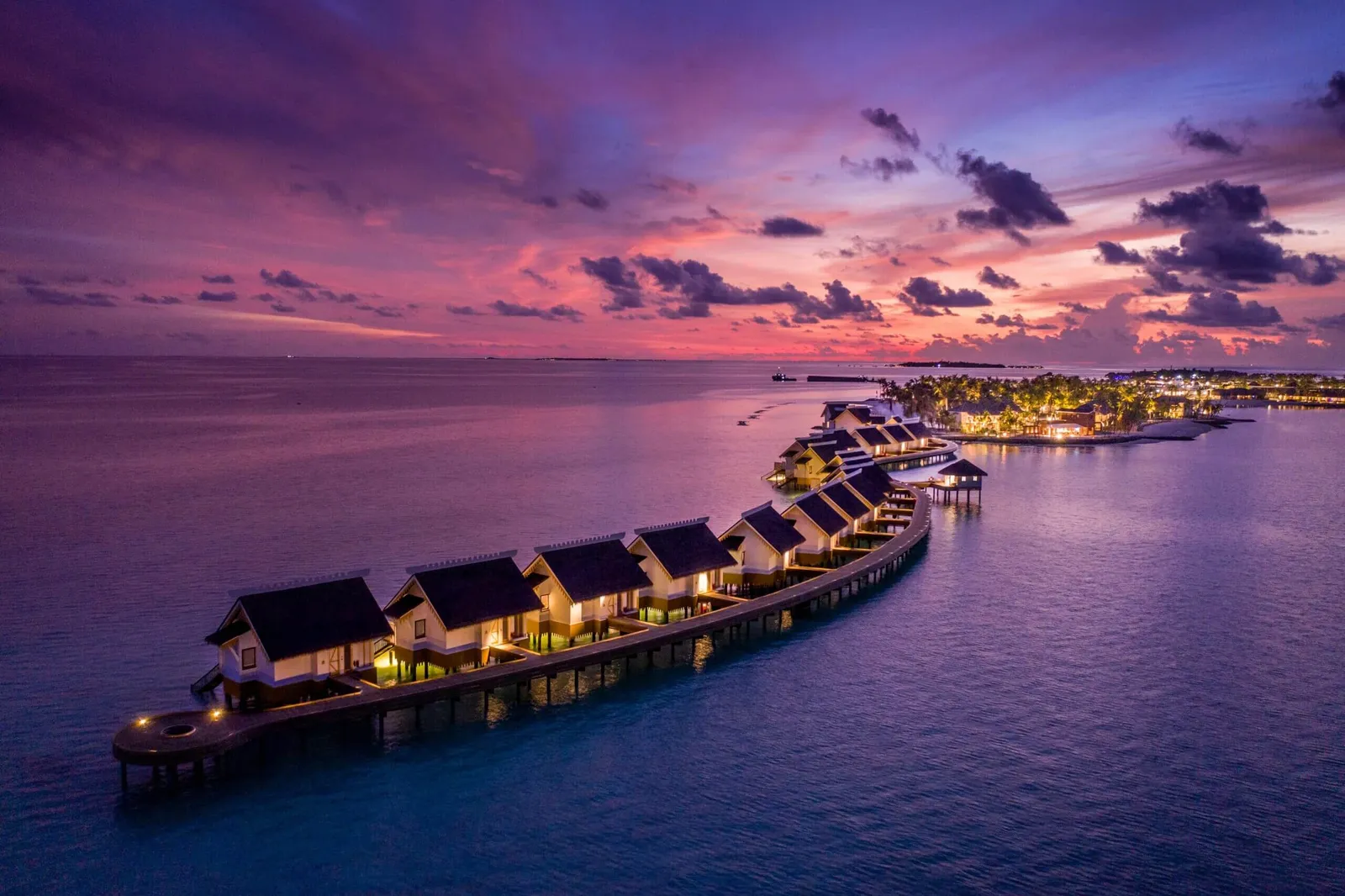 The water villas at dusk, their lights on under a violet sky