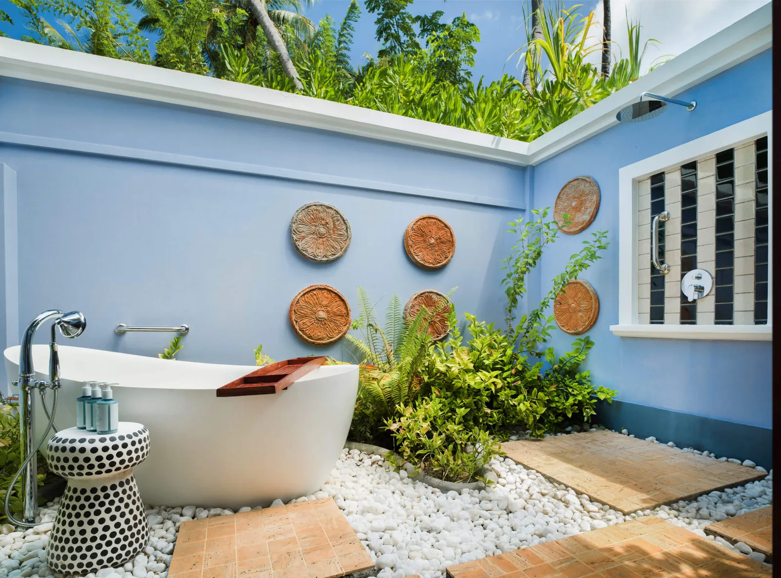 A Beach Villa’s outdoor bathtub, between pale-blue walls and plants