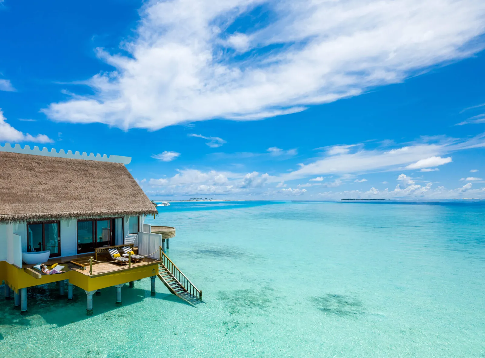 An Overwater Villa with its thatched roof above the turquoise lagoon, steps down into the water