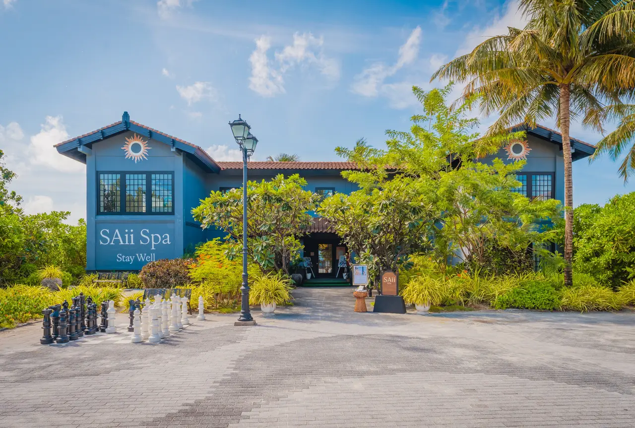 The blue 2-storey SAii Spa building and its sign, among palms and lamp posts