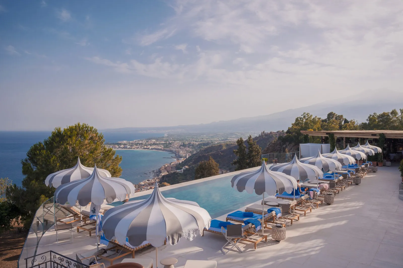 The pool and striped parasols above the Taormina coast