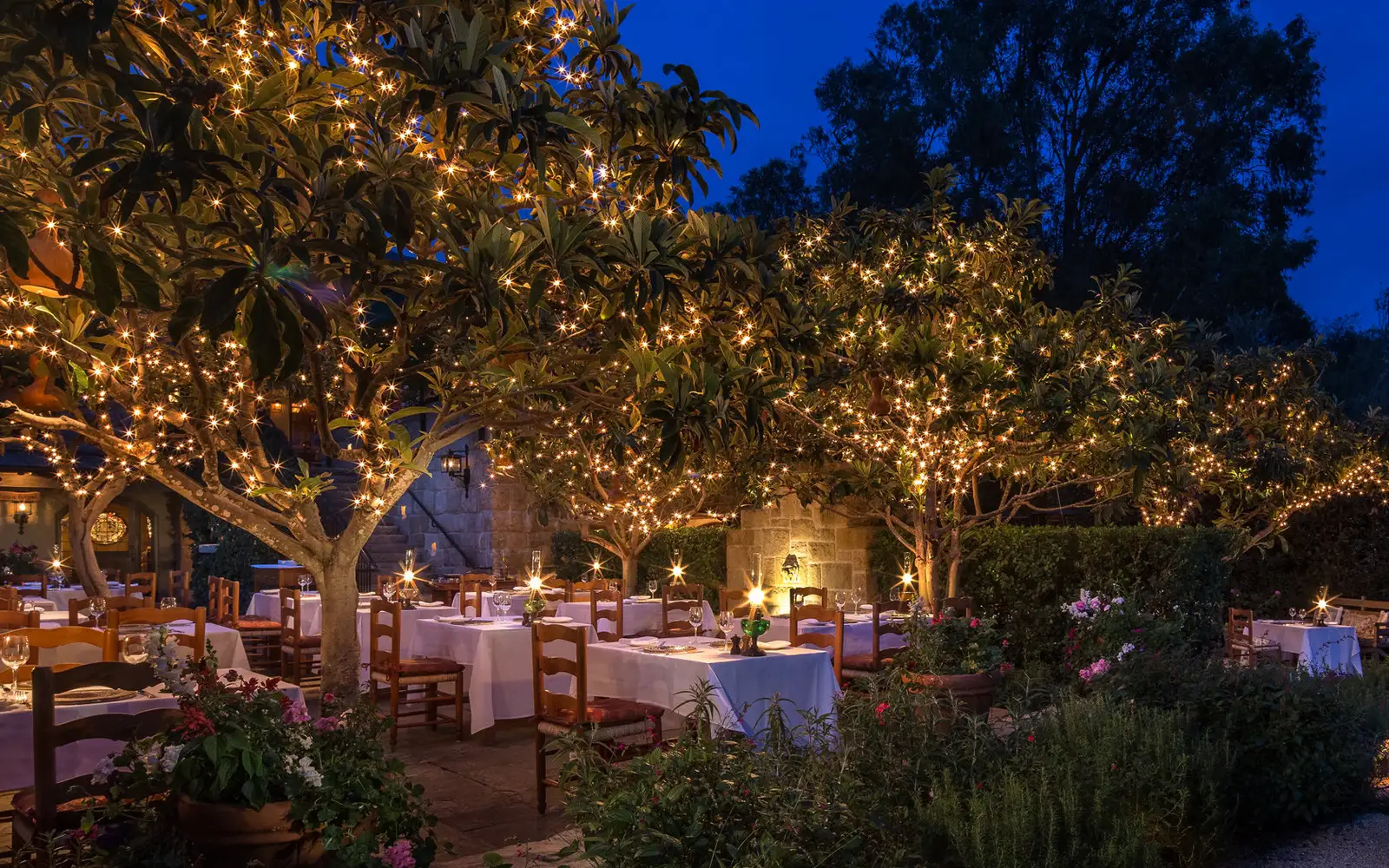 Stonehouse’s outdoor tables laid for dinner at dusk, under trees strung with fairy lights.