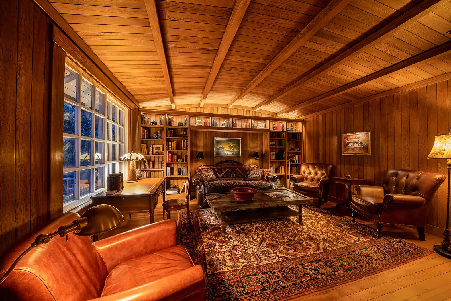 The wood-panelled library, with leather armchairs, rugs and bookshelves along the wall.