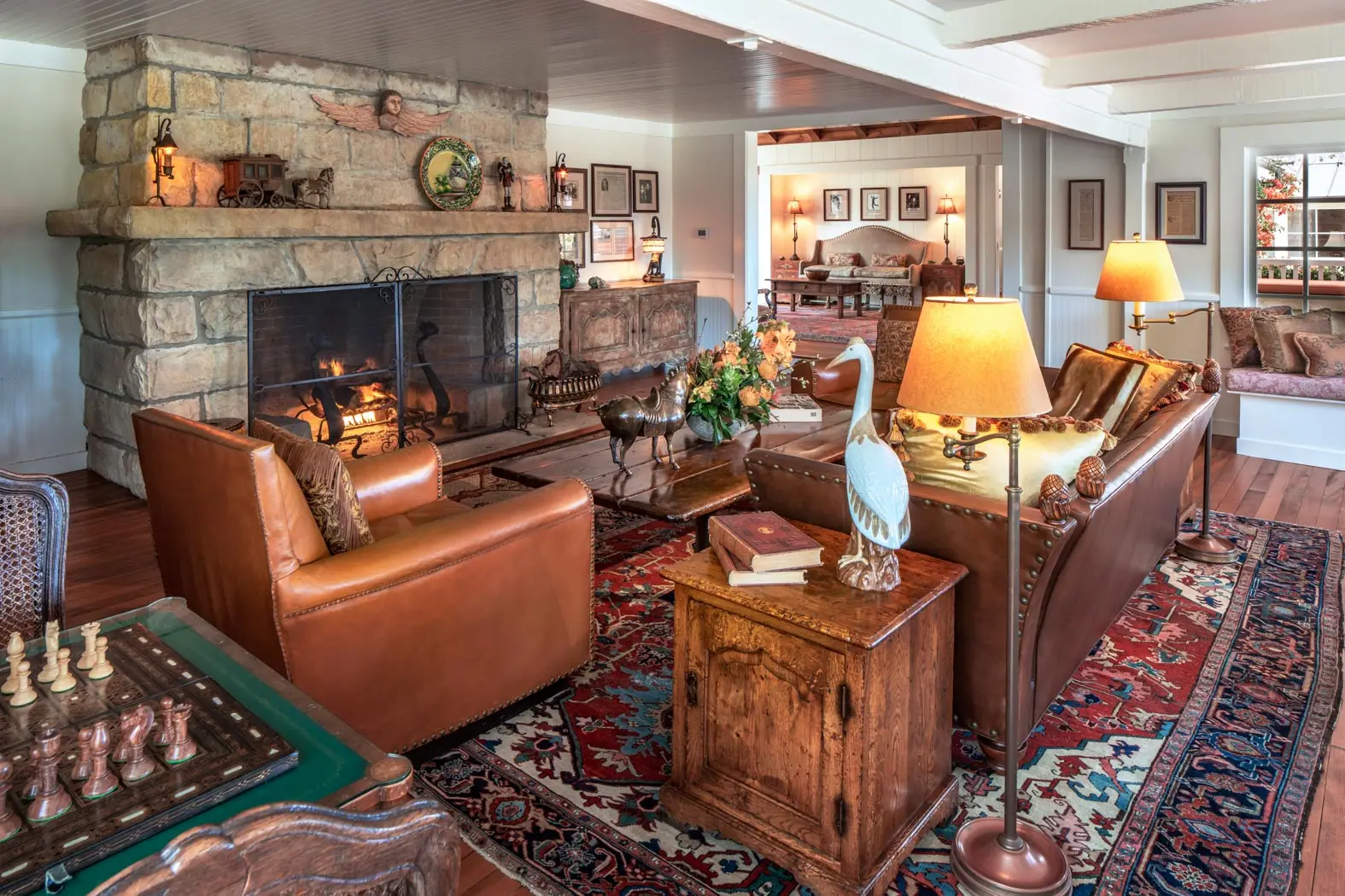 A sitting room with a lit stone fireplace, leather sofas, a chessboard and Persian rugs.