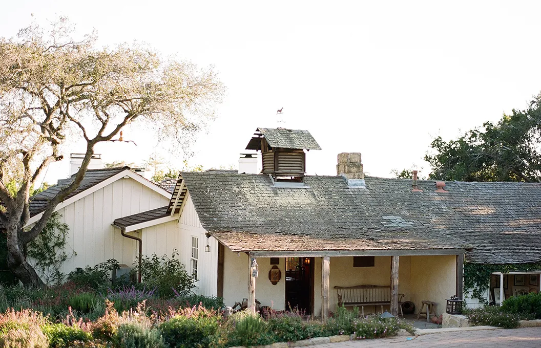 The Old Adobe, the low house of 1825 with its shingle roof and porch, among the oaks.