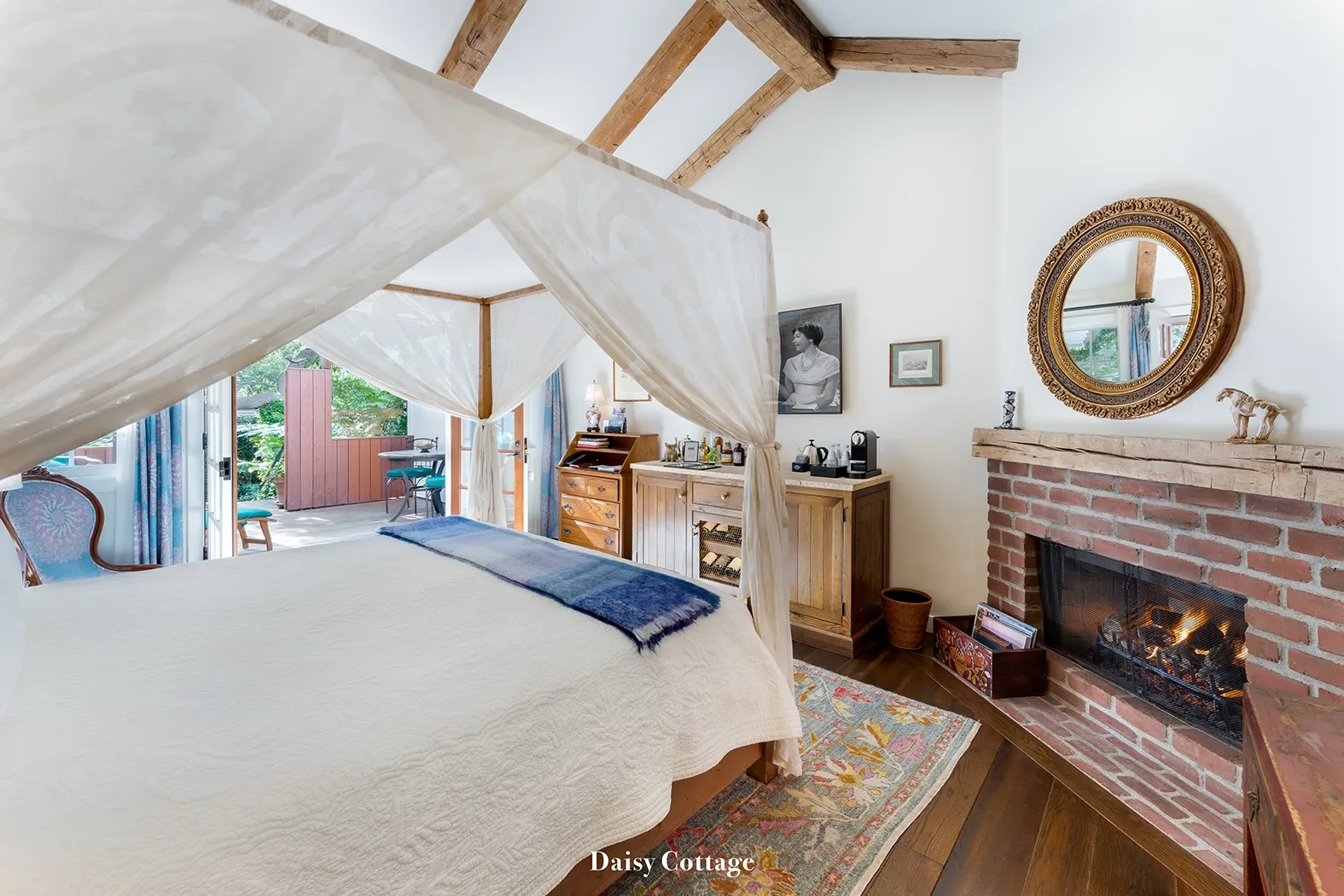 Daisy: the canopy bed with white drapes, the brick fireplace lit and a round mirror on the wall.
