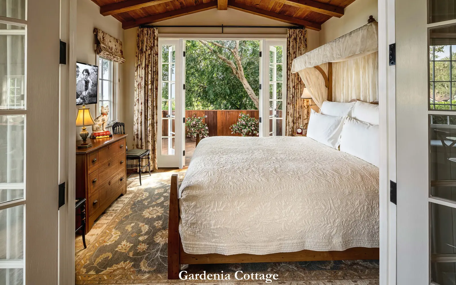 Gardenia: the bedroom seen through French doors, the bed under a white coverlet and the patio among trees beyond.