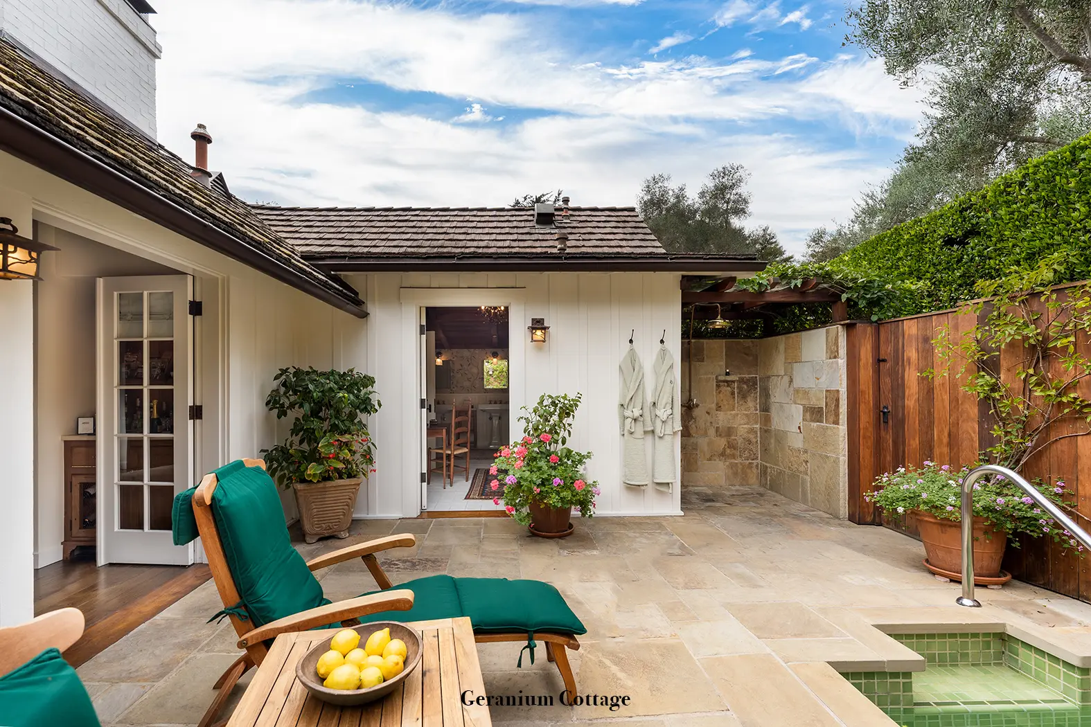 Geranium: the paved patio with a green lounger, the sunken spa, the stone outdoor shower and 2 robes hanging.