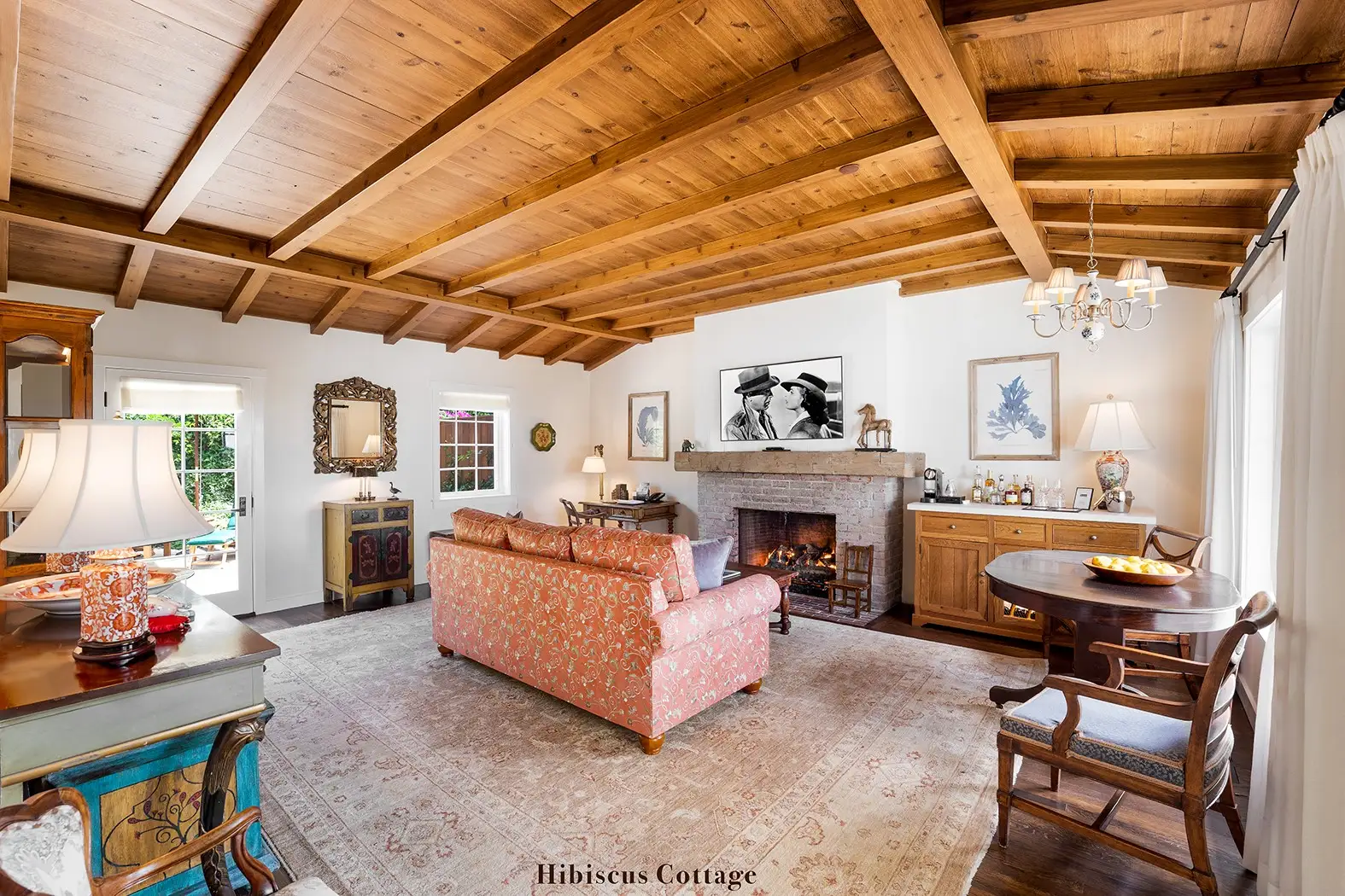 Hibiscus: the living room under a beamed ceiling, the fireplace lit, a salmon-coloured sofa and a round table.